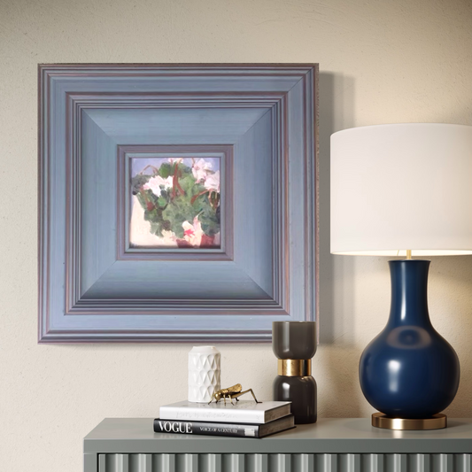 Small framed floral oil painting styled above a console table with a deep blue lamp and warm decorative accents in a refined contemporary interior.