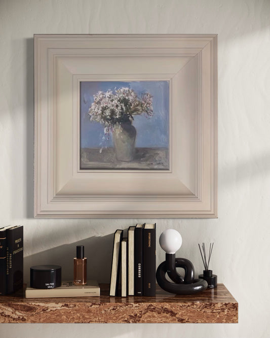 Small framed floral oil painting displayed above a wooden console table with books and sculptural decor in a serene contemporary interior.