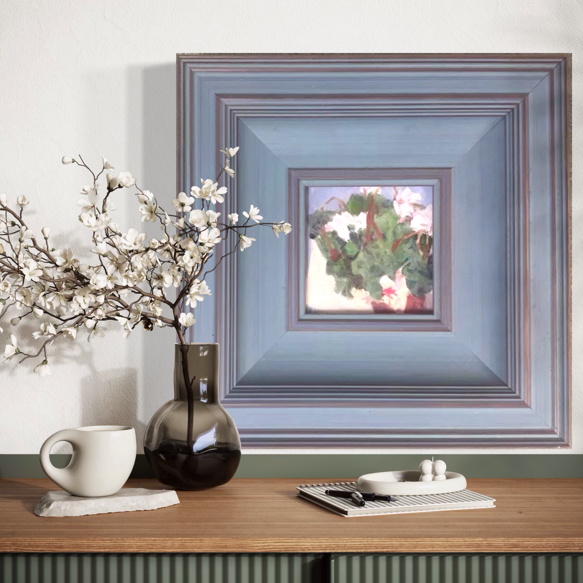 Small floral oil painting in a handcrafted blue gallery frame styled in a minimalist home interior with neutral ceramics and warm wood textures.