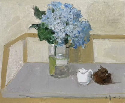 Detail of blue hydrangea flowers, glass vase, and decorative objects arranged within a minimalist interior setting.