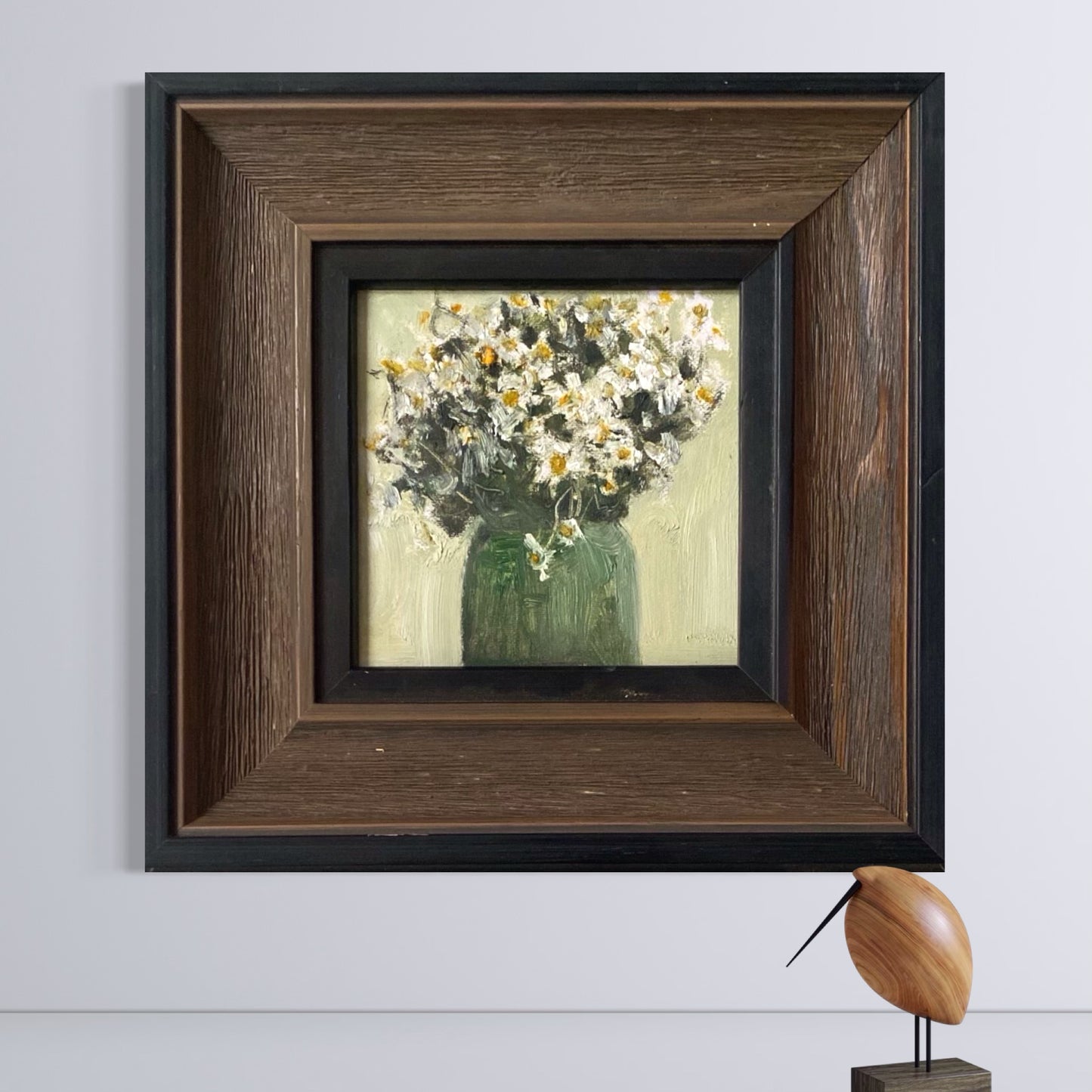 Small framed floral oil painting displayed on a neutral wall in a refined interior with soft natural lighting and warm wood tones.