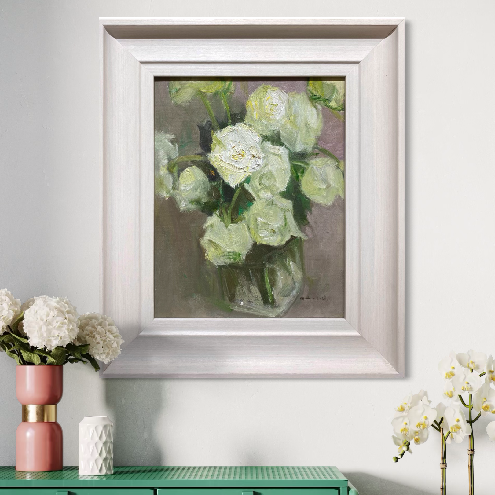 A framed original floral oil painting featuring white roses placed above a dark wooden cabinet. The composition adds warmth, softness, and quiet presence to the interior.