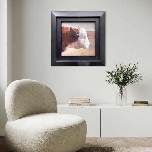A framed original cow portrait oil painting displayed in a minimalist living room with soft neutral tones and modern furniture, adding warmth, texture, and quiet character to the interior space.