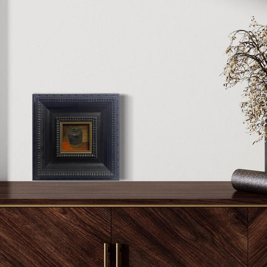 Small framed still life oil painting displayed above a modern wooden cabinet in a calm contemporary interior.