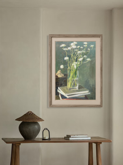 Original oil painting featuring white flowers in a glass vase displayed above a wooden cabinet, adding serenity and elegance to the interior space.