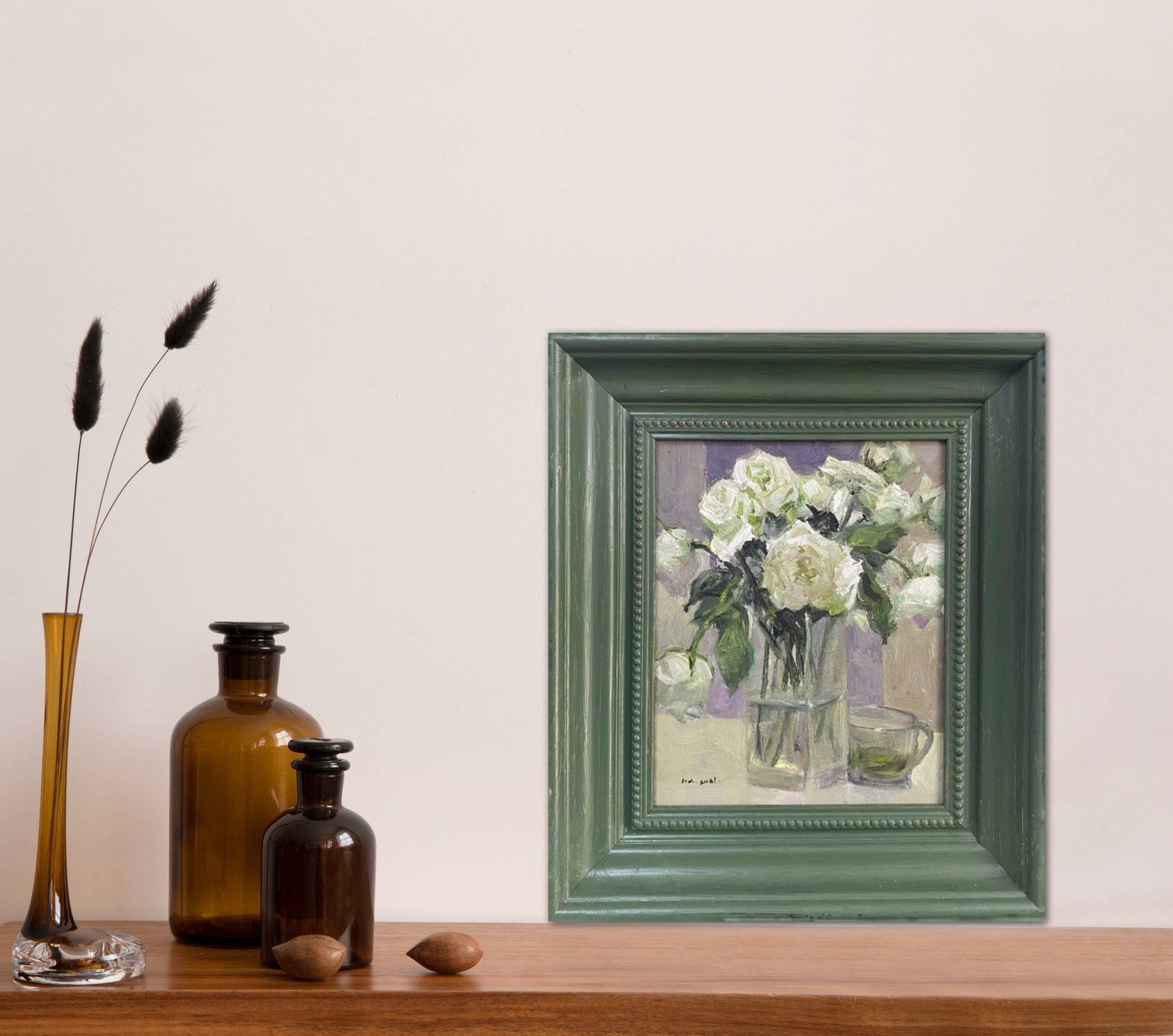 Original floral oil painting shown in a minimal interior setting. The muted green frame and soft floral composition create a peaceful atmosphere suited for contemporary living spaces.