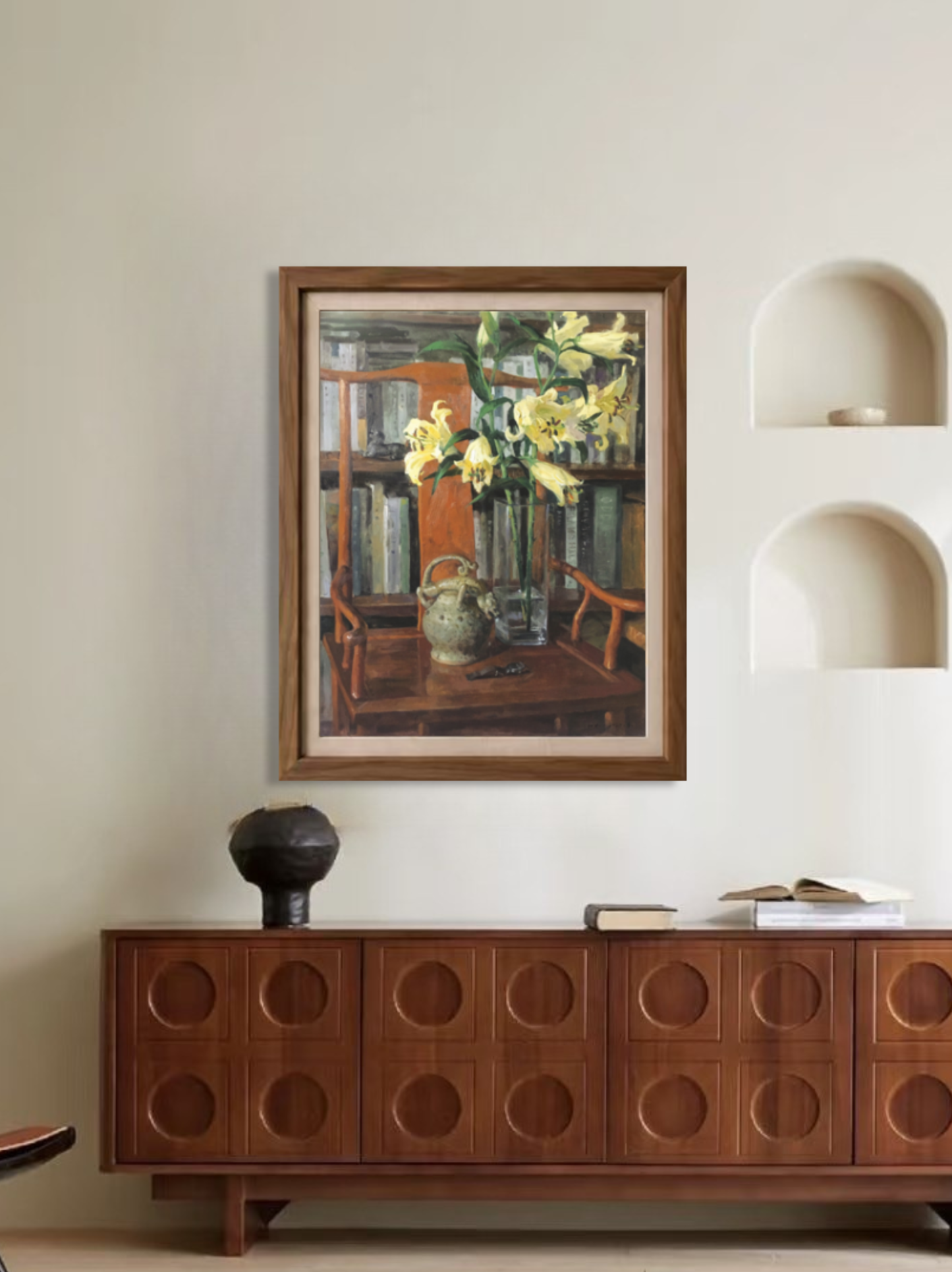 Framed original oil painting featuring lilies, books, and interior objects displayed above a wooden cabinet, creating a refined focal point for home decor.