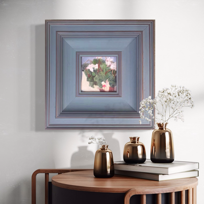 Original floral oil painting in a muted blue frame displayed in a calm interior with soft lighting, sculptural decor, and dried botanical elements.