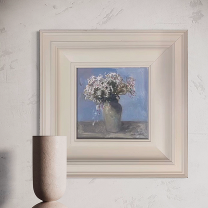 Small floral oil painting framed in cream-toned wood, displayed against a refined neutral wall with modern interior styling.