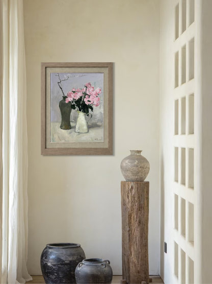 Framed oil painting featuring pink flowers in ceramic and glass vases displayed by a window, creating a soft, serene focal point for interior decor.