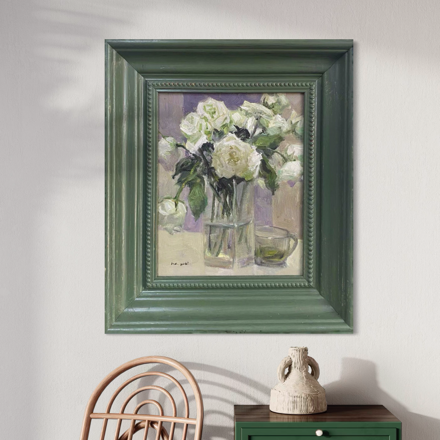 A framed oil painting of white roses placed beside simple ceramic and glass objects. The composition adds softness, balance, and a collected interior mood.