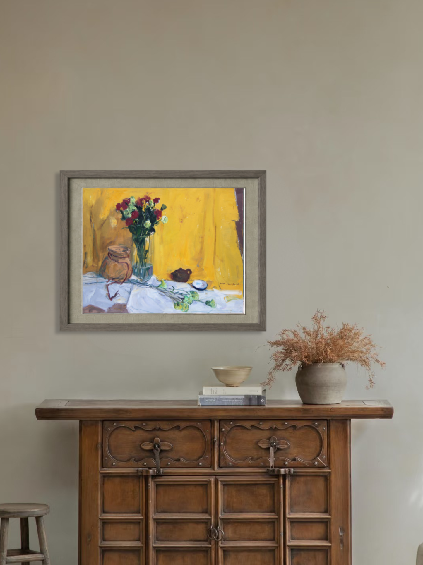 Framed oil painting featuring red flowers in a glass vase displayed above a wooden cabinet, creating a vibrant focal point within the space.