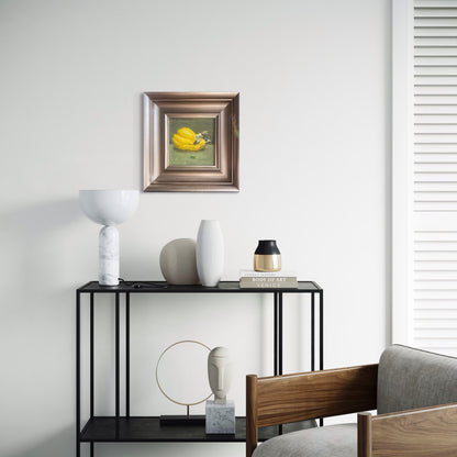 A small framed still life oil painting displayed within a modern home setting featuring soft lighting and minimal decor, adding warmth and quiet visual focus to the interior space.