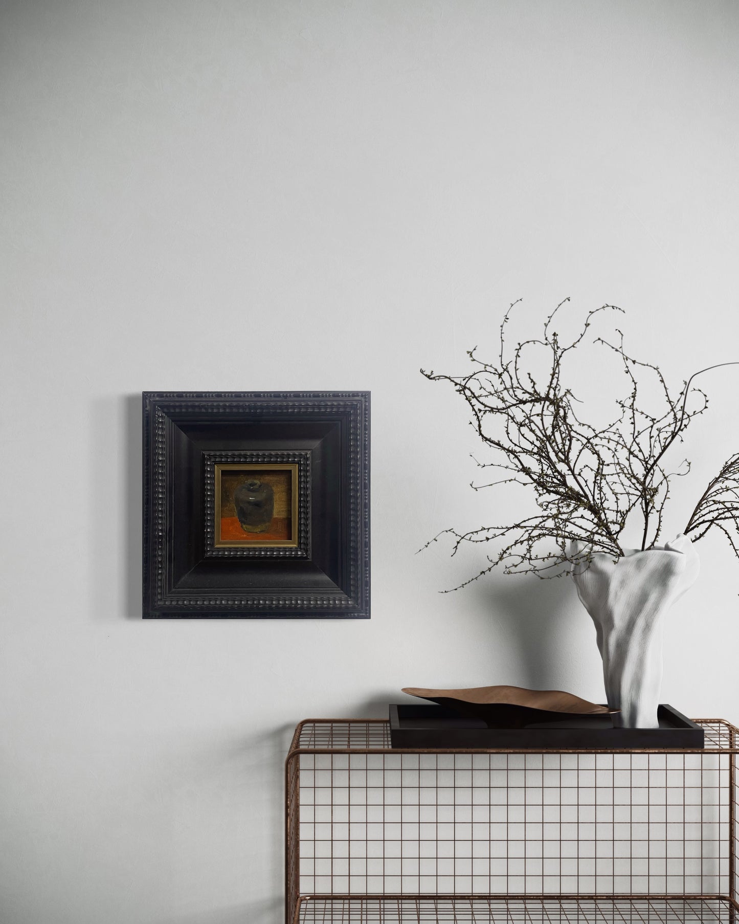 Small classical still life painting in a deep black frame displayed on a neutral wall with soft natural lighting and refined interior styling.