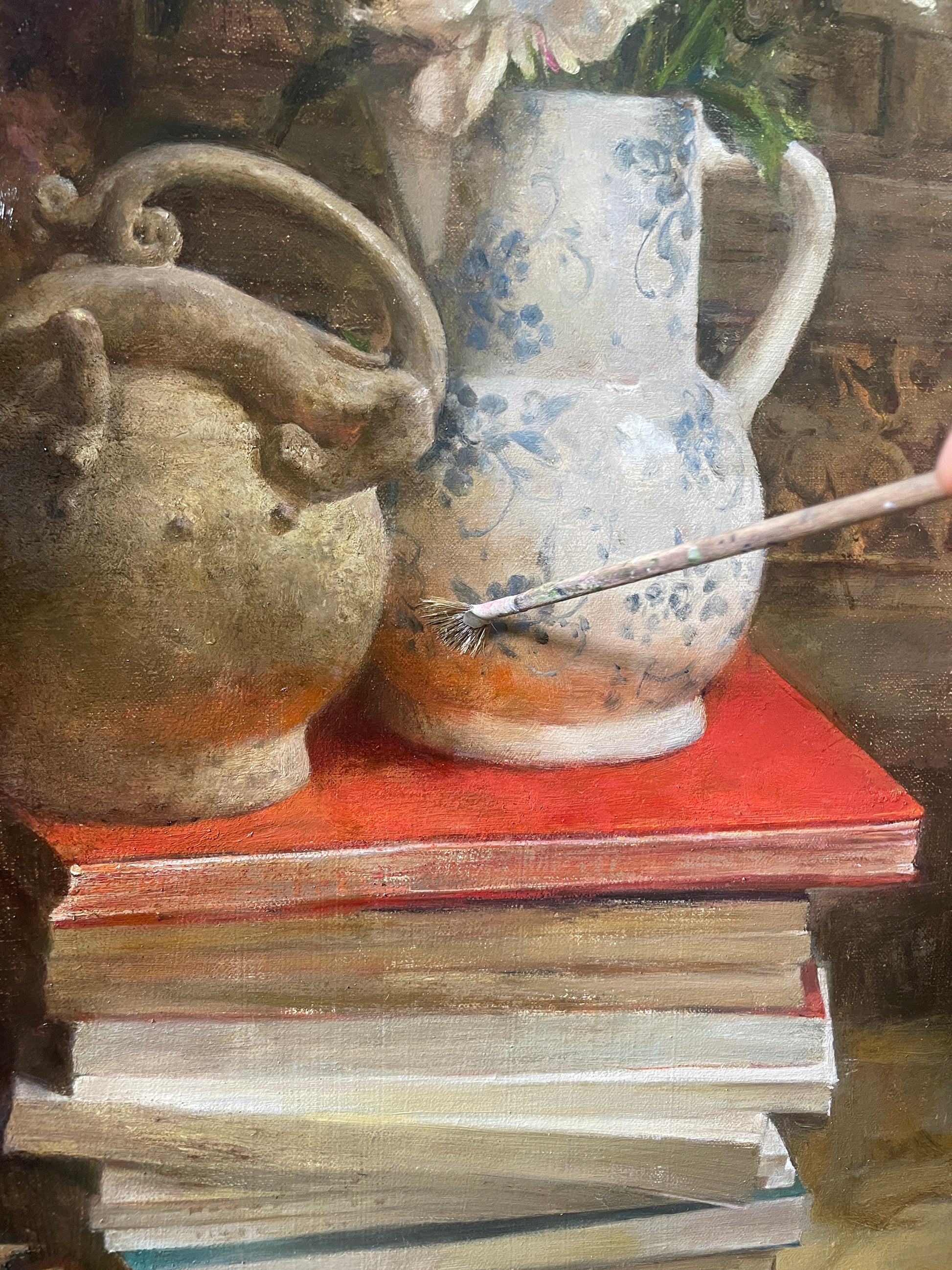 Detail showing a ceramic vase resting on stacked books within the still life composition.